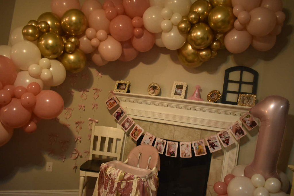 Blush, white and chrome gold balloon garland sweeping across a mantel for a first birthday