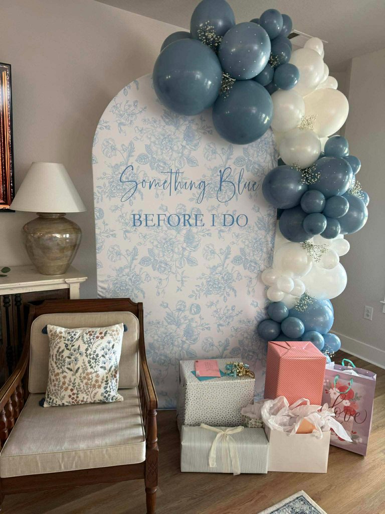 Dusty blue and white balloon garland over a blue toile arch backdrop for a bridal shower